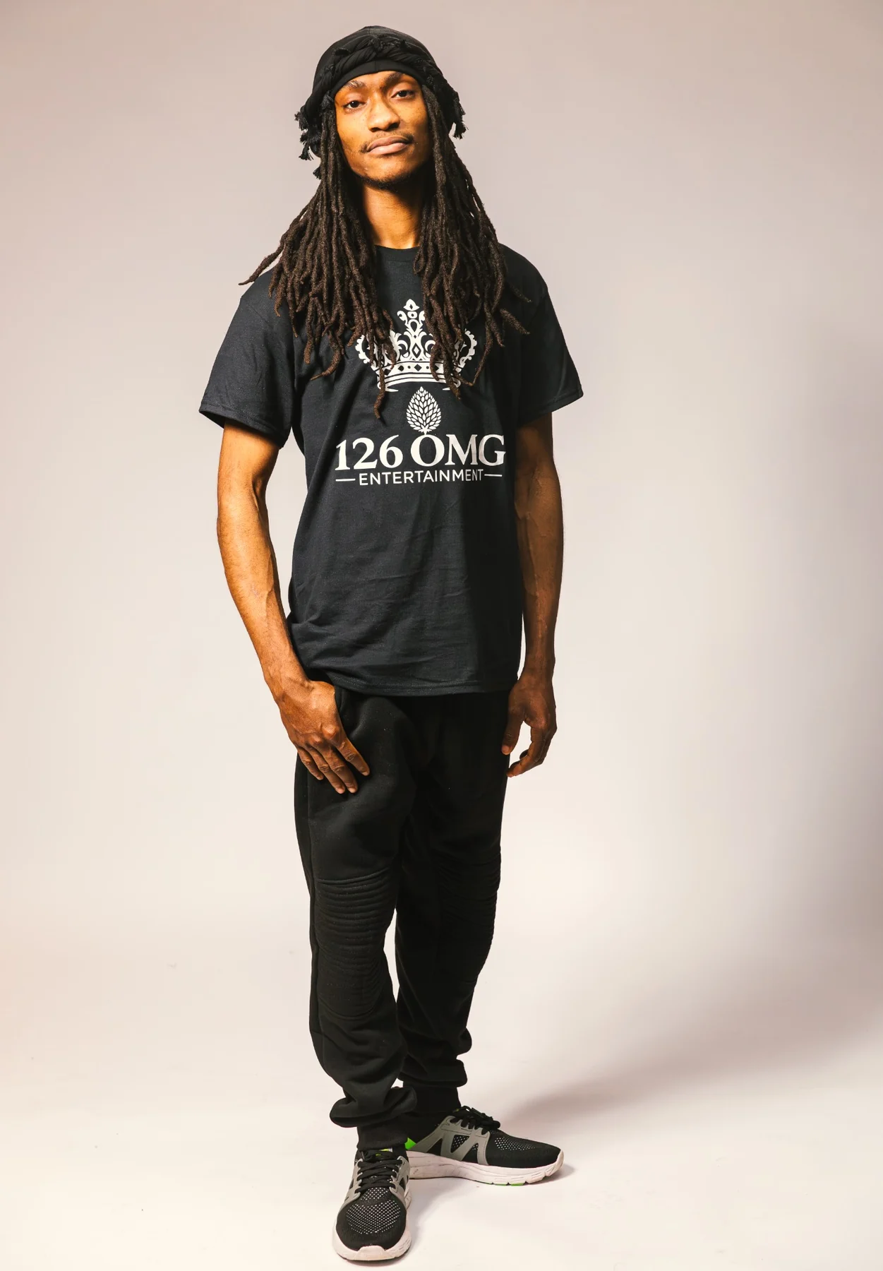 A son in a 126 OMG Entertainment shirt, layered necklaces, and dark sneakers