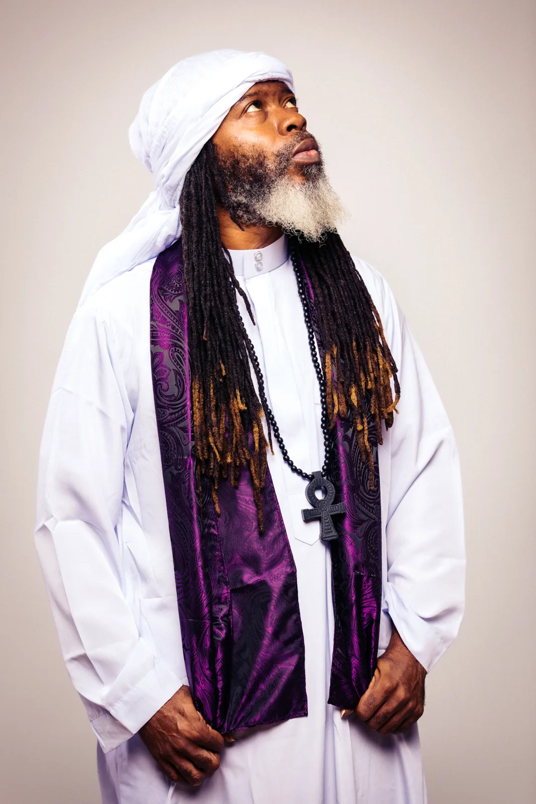 CITYSLIC THE OG looking upward in a white headwrap and purple scarf