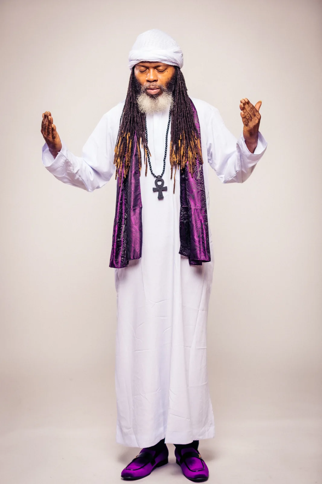 CITYSLIC THE OG in white and purple with his hands raised in prayer